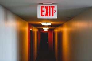 exit sign in a lit up long hallway exit to right from eerie hallway