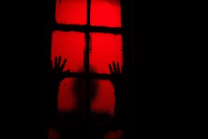 silhouette of person leaning against window in room with red light